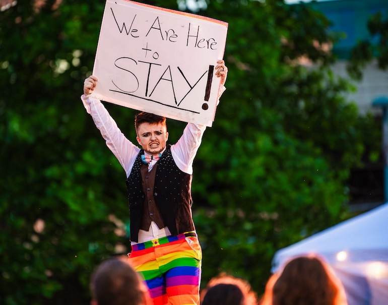 Logan Flynn-Monroe with sign reading "We Are Here to Stay" during Pride Party at Bass Street Landing June 15.